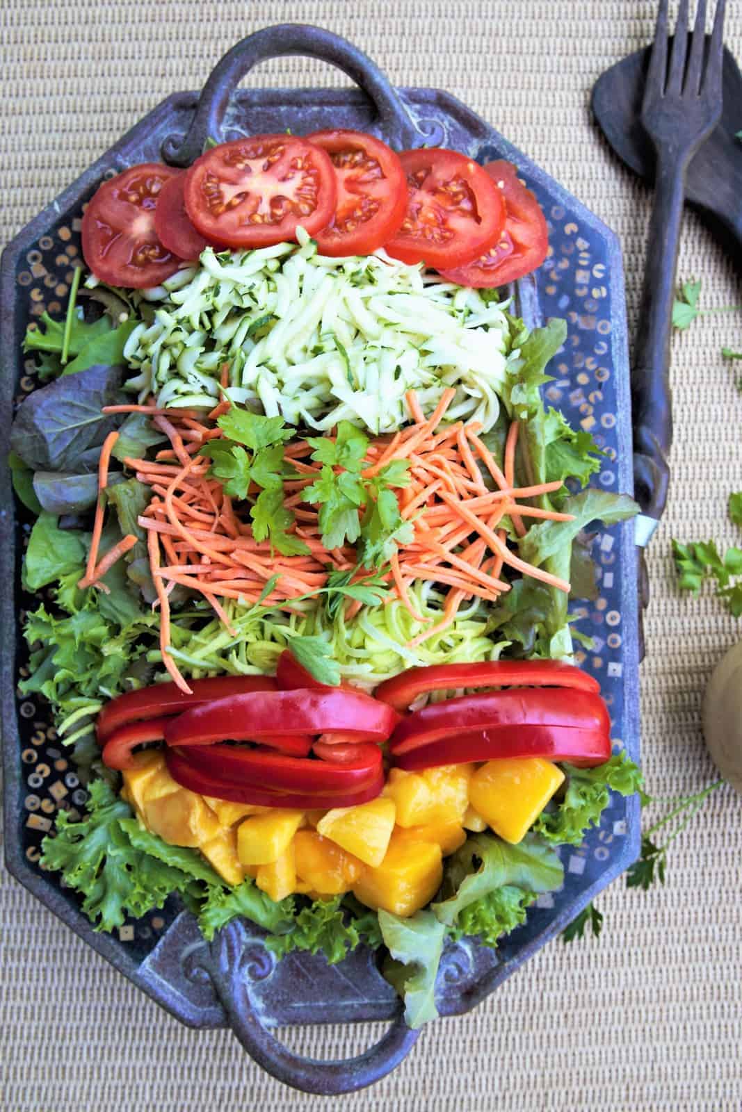 Fresh colorful vegetable salad with tomatoes, cucumbers, shredded carrots, diced mango, and leafy greens on a decorative tray, emphasizing healthy eating and vibrant food presentation.